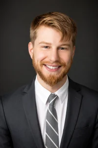 Professional corporate headshot of client Chris Maltby wearing a suit and tie against a dark studio background.