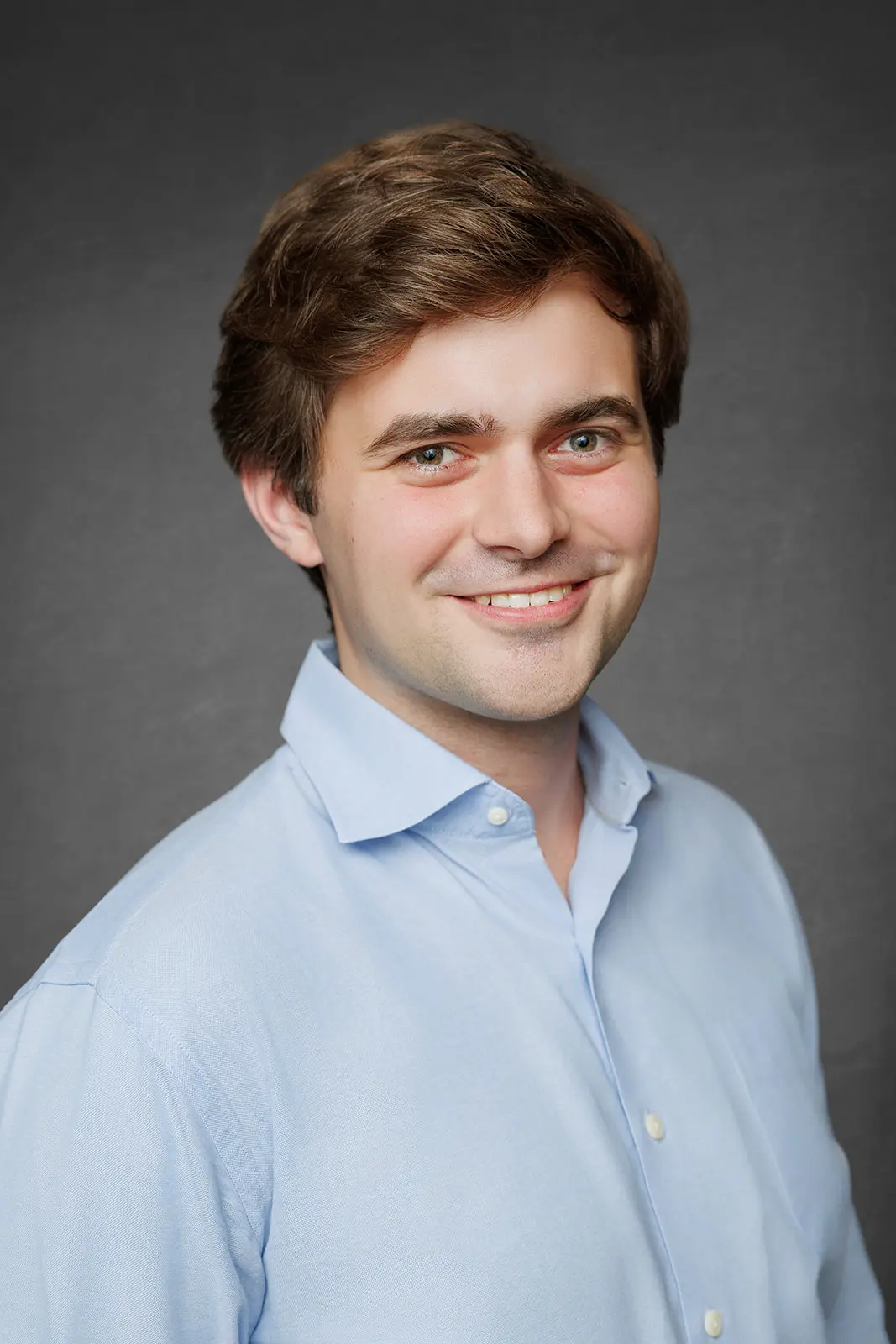 Professional business headshot of a man photographed against a gray studio backdrop.
